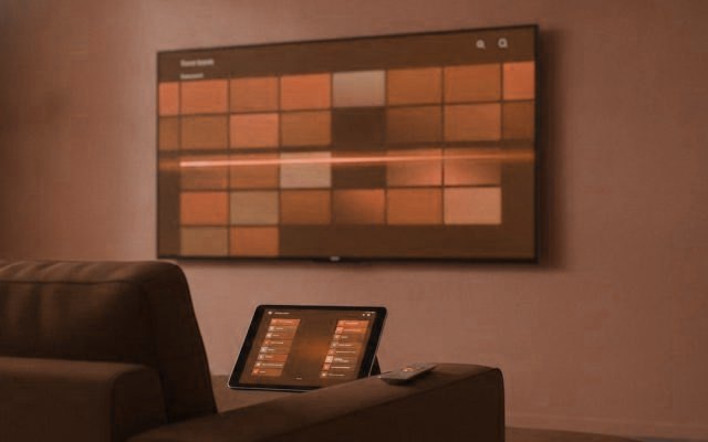 A TV showing a programme guide grid with a tablet and phone showing channel lists on a sofa