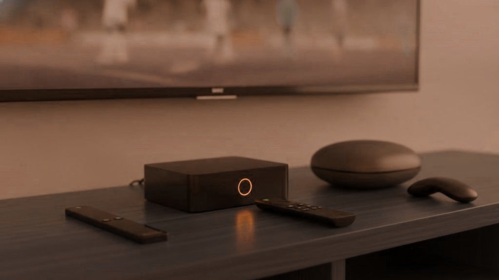 A streaming stick, a set-top box and a round streaming box with their remotes on a TV console