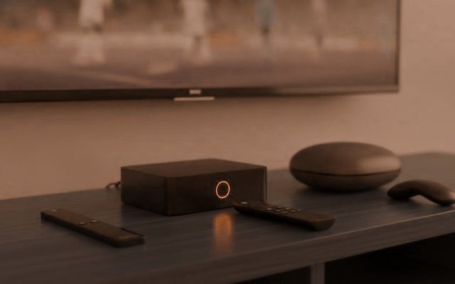 A streaming stick, a set-top box and a round streaming box with their remotes on a TV console