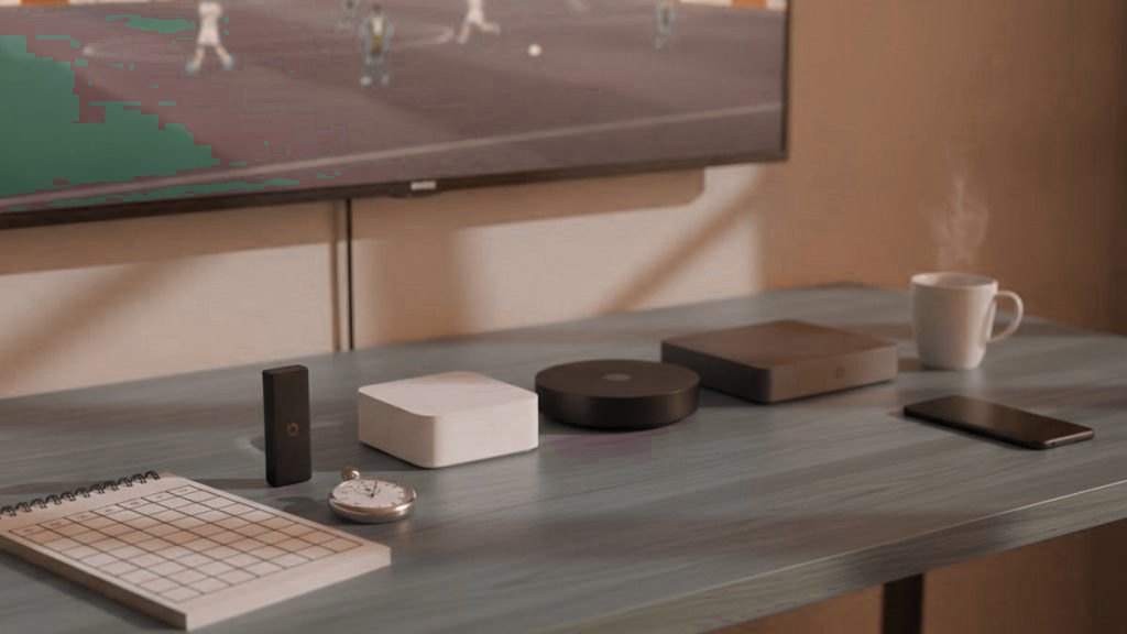 Five streaming devices, a notebook scoring grid and a stopwatch in front of a TV showing a football match
